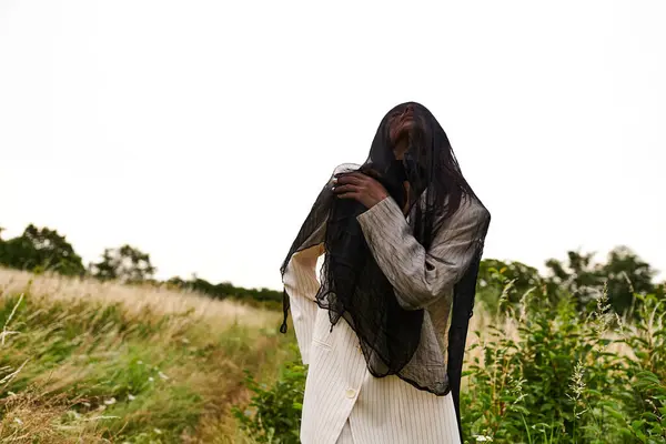 Молодая женщина в белом наряде изящно стоит на поле высокой травы, обнимая мягкий летний бриз. — стоковое фото