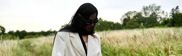 Молодая женщина в белом одеянии и черной вуали мирно стоит в поле высокой травы, обнимая летний ветерок. — стоковое фото