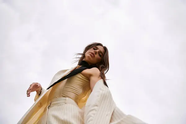 A young woman exudes confidence in a white suit and black tie, standing gracefully in a sunlit field. — Photo de stock