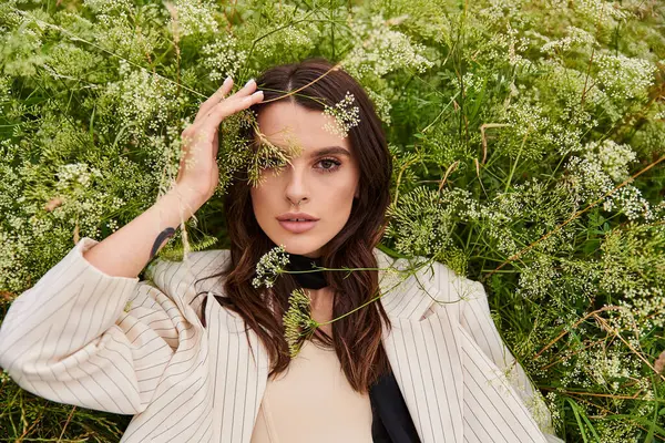 Una hermosa joven vestida de blanco yace en la hierba verde, con las manos suavemente apoyadas sobre su cabeza bajo el cálido sol de verano.. - foto de stock