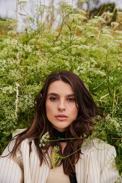 Красивая молодая женщина в белом наряде изящно стоит на поле высокой травы, обнимая мягкий летний бриз. — стоковое фото