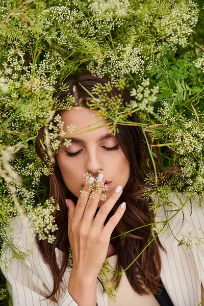 A beautiful young woman in white attire, hands on face, surrounded by a vibrant array of flowers in a sunlit field. — Photo de stock