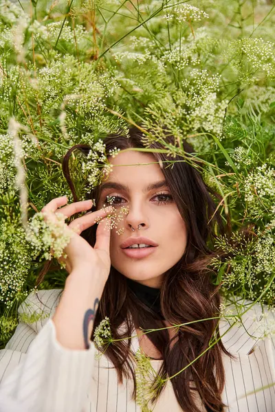 Una joven vestida de blanco se levanta con gracia en un campo de plantas verdes vibrantes, abrazando la brisa del verano. - foto de stock
