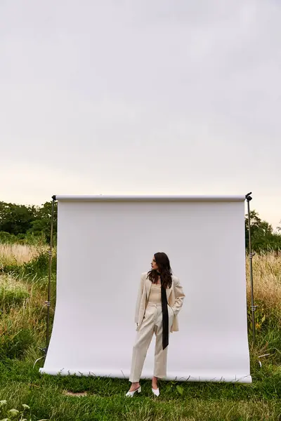 Una bella giovane donna in abito bianco si erge con grazia di fronte a uno sfondo bianco, godendo la brezza estiva. — Foto stock