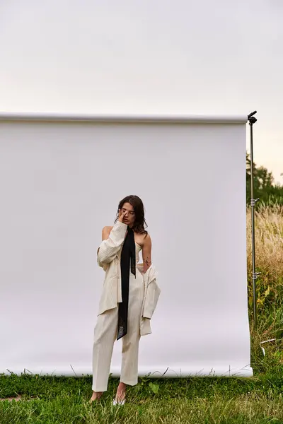 Una bella giovane donna in abito bianco in piedi con grazia di fronte a uno sfondo bianco, godendo la brezza estiva. — Foto stock