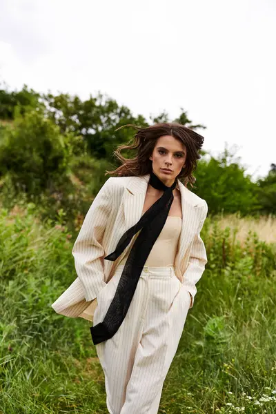 A beautiful young woman in a white suit and black tie stands confidently in a field, feeling the summer breeze. — Stock Photo