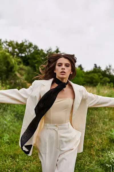 A beautiful young woman in a white suit and black tie enjoying the summer breeze in a field of nature. — Stock Photo