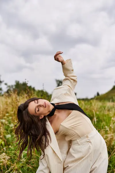 Una bella giovane donna in abito bianco e cravatta nera godersi la brezza estiva in un campo. — Foto stock