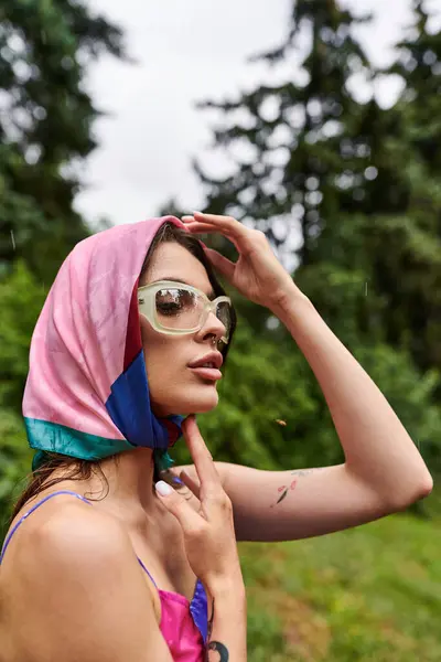A beautiful young woman in a vibrant pink and blue scarf and stylish sunglasses, enjoying the summer breeze in nature. — Stock Photo