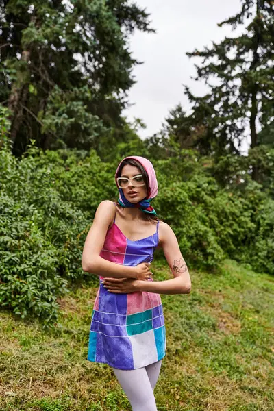 Una joven con un vestido colorido y gafas de sol bailando con gracia en un campo vibrante, disfrutando de la brisa del verano. - foto de stock