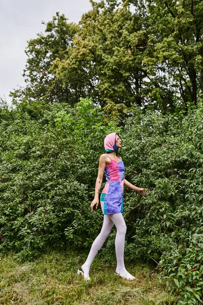 Una giovane donna in un abito colorato e sciarpa testa, abbracciando la brezza estiva nella natura. — Foto stock