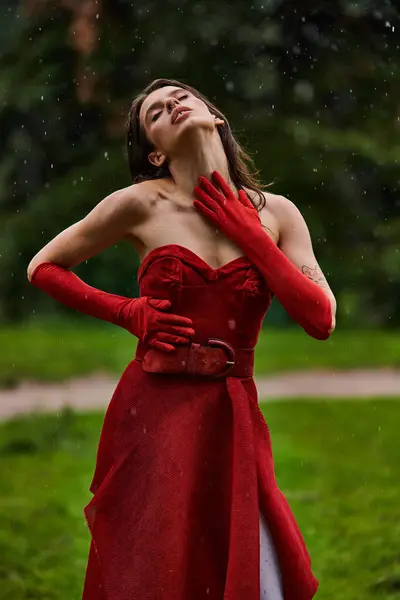 A young woman exudes elegance in a red dress and long gloves, immersed in the summer breeze of nature. - foto de stock