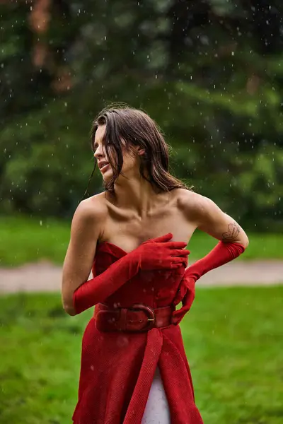 Eine verführerische junge Frau in rotem Kleid und langen Handschuhen genießt eine sommerliche Brise in der Natur. — Stockfoto