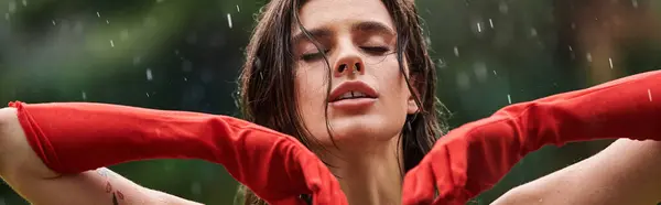 Eine junge Frau in roten langen Handschuhen steht selbstbewusst, die Hände auf den Hüften, umarmt den Regen. — Stockfoto