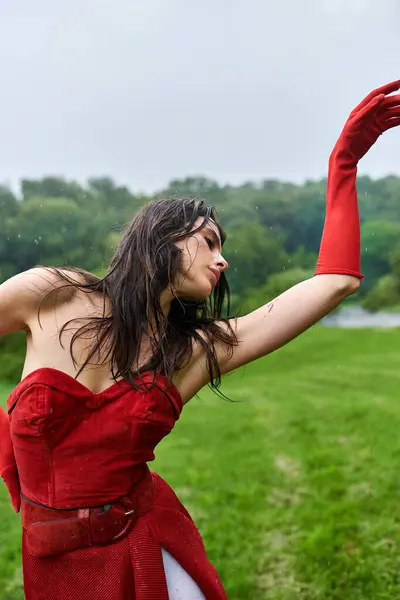 Una joven atractiva con un vestido rojo y guantes largos, disfrutando de una brisa veraniega en un entorno natural. - foto de stock
