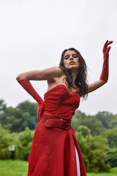 Beautiful young woman in a red dress and long gloves standing gracefully in a serene field, enjoying the summer breeze. — Stock Photo