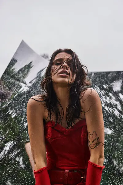 A mesmerizing scene unfolds as a young woman in a striking red dress and long gloves stands gracefully against a backdrop of a mountain. — Photo de stock