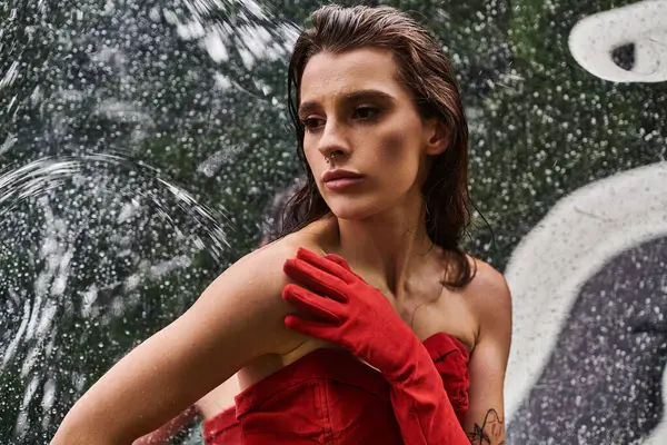 A beautiful young woman in a red dress and long gloves enjoys the summer breeze by a fountain. — Photo de stock