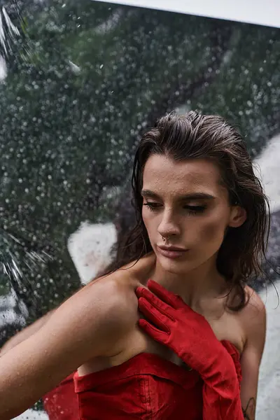 Молодая женщина в красном платье и длинных перчатках изящно стоит под дождем, наслаждаясь летним бризом на природе. — стоковое фото