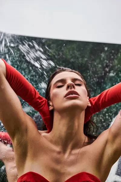 Eine attraktive junge Frau in einem fließenden roten Kleid und langen Handschuhen entspannt sich mit den Händen hinter dem Kopf und genießt die sommerliche Brise in der Natur. — Stockfoto