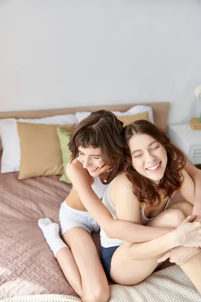 Two women in cozy attire sit on a bed, hugging each other warmly. — Stock Photo