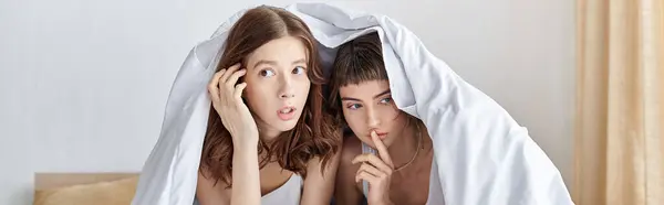 Two women seek refuge under a cozy blanket. — Stock Photo