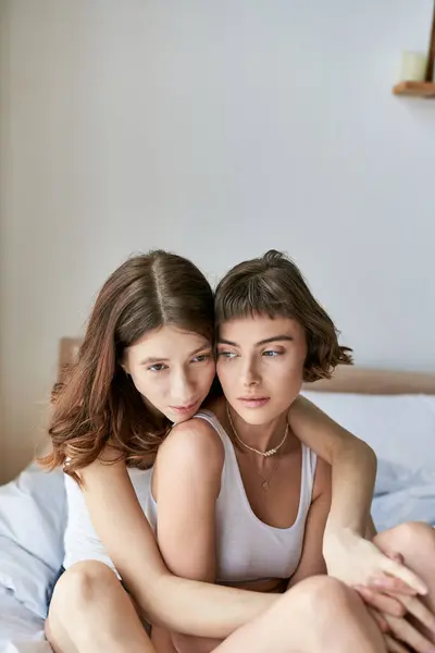 Una pareja lesbiana con un atuendo acogedor disfrutando de un momento tranquilo sentada en una cama. - foto de stock