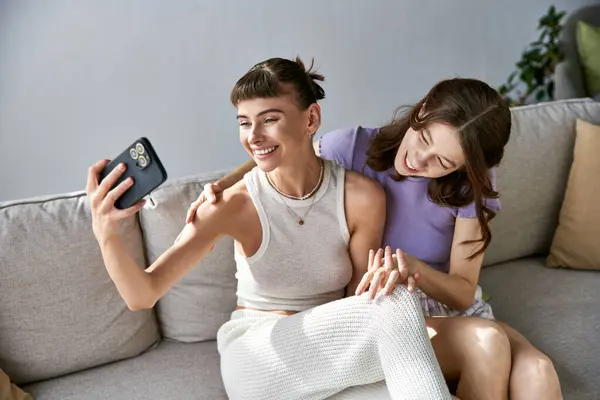 Dos mujeres en traje cómodo sentadas en un sofá, absortas en un teléfono celular. - foto de stock