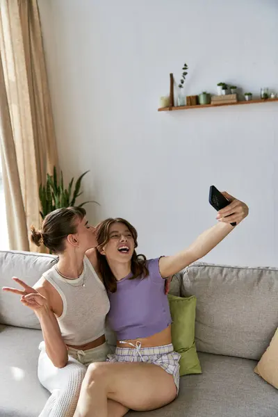 A beautiful lesbian couple relaxes on a couch, one holding a remote control. — Stock Photo