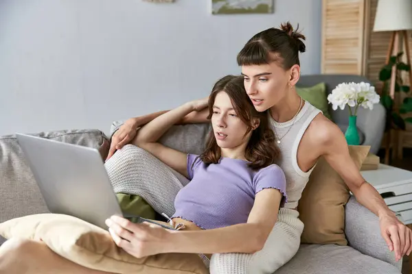 Two women relax on a couch, working together on a laptop. — Stock Photo