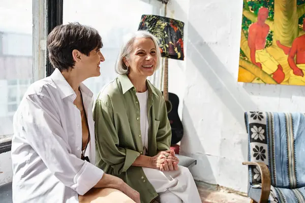 Two mature women sit closely in an art studio. — Stock Photo
