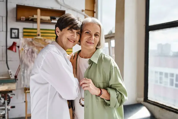 A mature lesbian couple standing together in an art studio. — Stock Photo