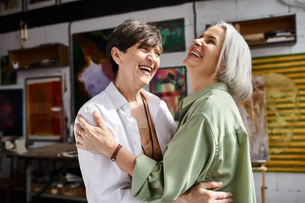 A mature lesbian couple hugging tenderly in an art studio. — Stock Photo