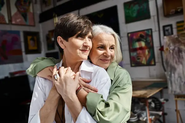 Two women tenderly embrace in an art studio. — Stock Photo