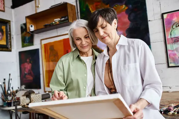 Una pareja de lesbianas maduras admiran las obras de arte juntas en un estudio. - foto de stock