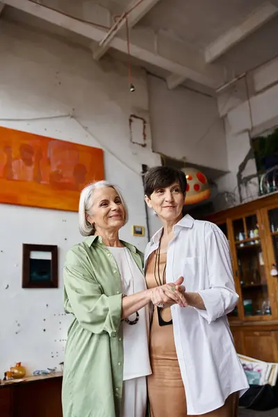 Two mature women, standing in an art studio, exude a sense of togetherness. — Stock Photo