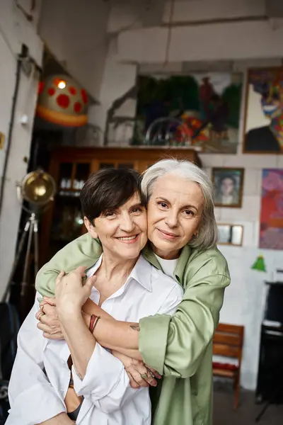 Two mature women hug each other in a cozy art studio. — Stock Photo