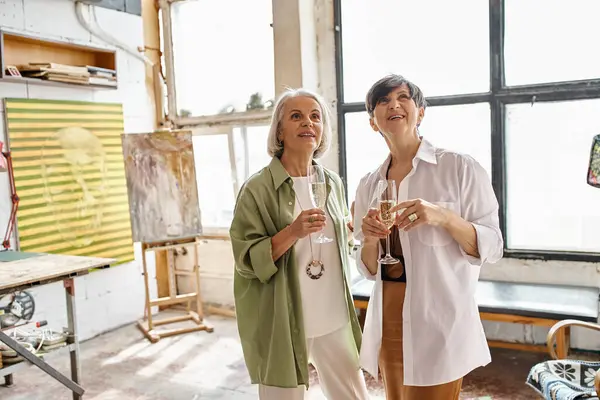 Two mature women, a loving couple, stand side by side in an art studio. — Stock Photo