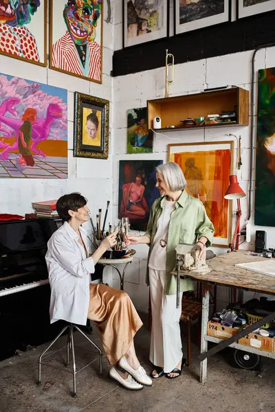 Deux femmes posant paisiblement entourées de peintures dans un atelier d'art. — Photo de stock