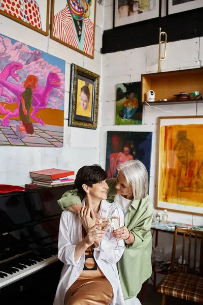 Dos mujeres, lesbianas maduras, de pie junto a un piano de cola en un estudio de arte. - foto de stock