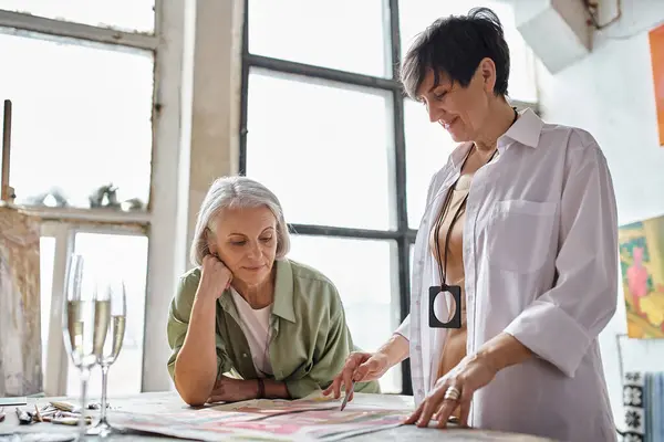 Una coppia lesbica matura si gode il tempo insieme in uno studio d'arte; uno in piedi, uno seduto. — Foto stock