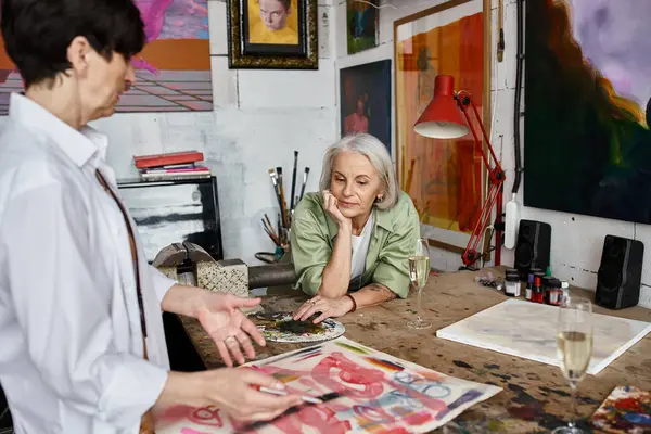 Una pareja de lesbianas maduras admira una obra de arte en un estudio. - foto de stock