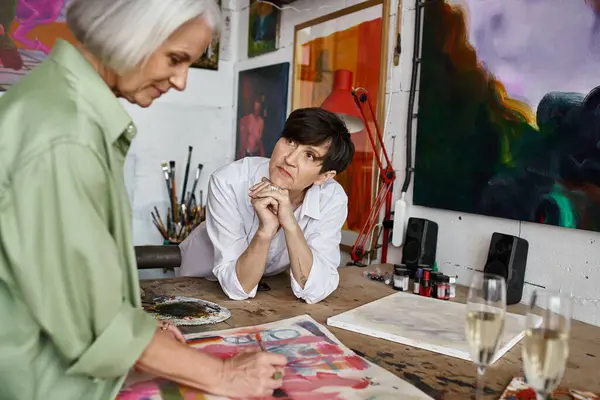 A woman is seated at a table in front of a captivating painting in an art studio. — Stock Photo