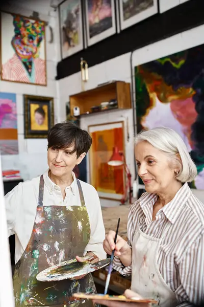 A mature lesbian couple paint in an art studio. — Stock Photo