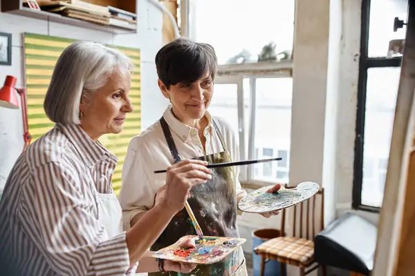 Two women immersed in creativity, paint with a brush and palette in an art studio. — Stock Photo
