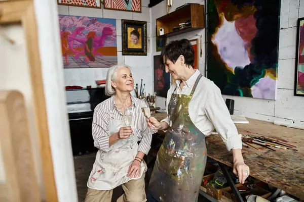 Two women, a mature lesbian couple, are immersed in art creation in a colorful studio. — Stock Photo