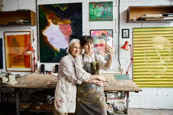 Two mature women, a couple, standing together in an art studio. — Stock Photo