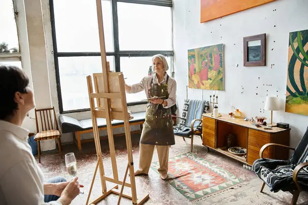 Woman standing at easel holding wine glass, painting partner. — Stock Photo