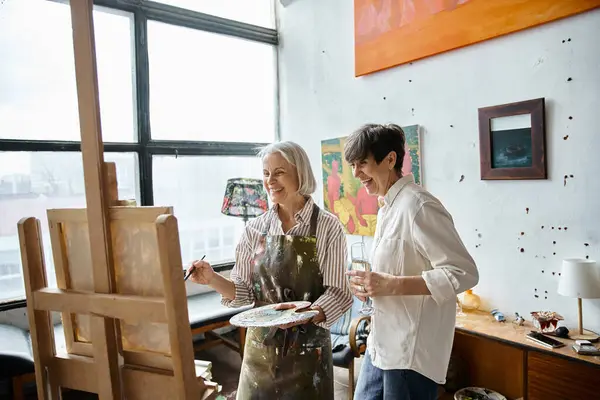 Two women, mature and in love, stand together in an art studio. — Stock Photo