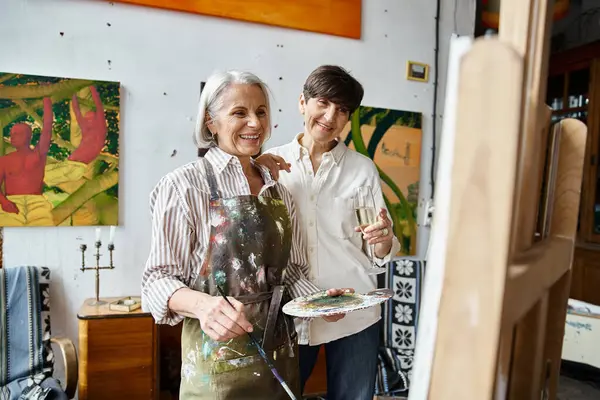 A mature lesbian couple stands in an art studio, sharing a moment of togetherness. — Stock Photo